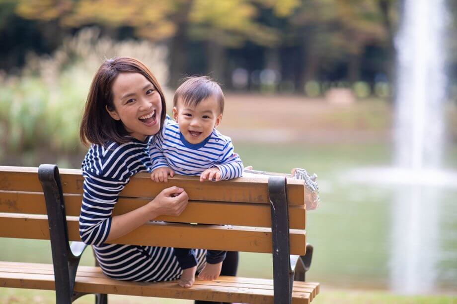 Mom and toddler, both wearing navy and white striped shirts, sitting on park bench, smiling