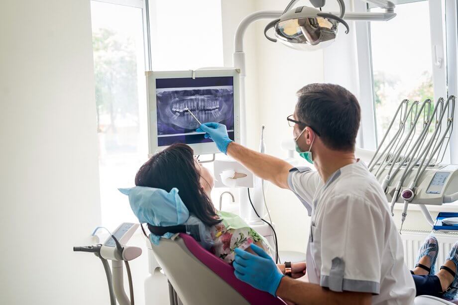 dentist with patient in dental chair pointing to x-ray on screen