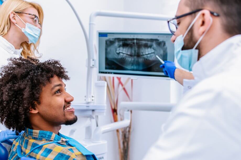 dentist points out digital x-ray to smiling patient in dental chair