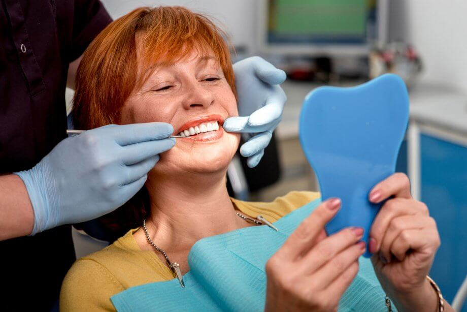 woman in dental chair looking in mirror as dentist points to her teeth